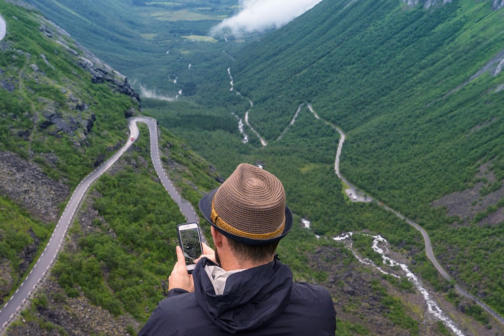 A Man Holds His Phone Above the Trollstigen in Norway