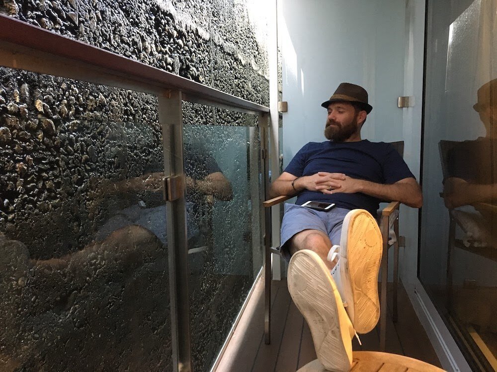 A man sits on the terrace of a river cruise ship in the Iron Gate Gorge and Lock. The Lock fills the view, and can be touched from the boat