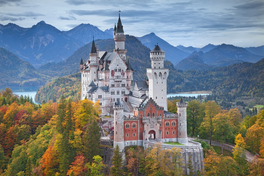 newchwanstein castle in Germany—castle on a hill surrounded by tall trees and a lake