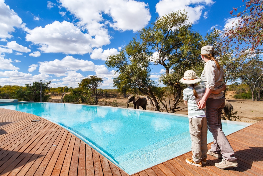 Family of mother and child on African safari vacation enjoying wildlife viewing standing near swimming pool