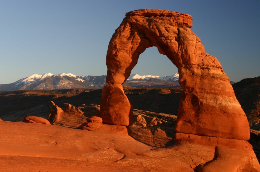 red rock delicate arch in arches national park with mountains in the background