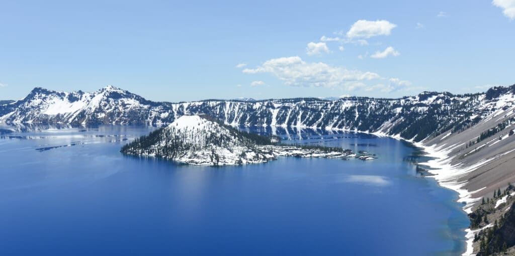 Clear blue water of Crater Lake National Park in Oregon during early spring with some snow left from winter. Wizard Island in the distance.