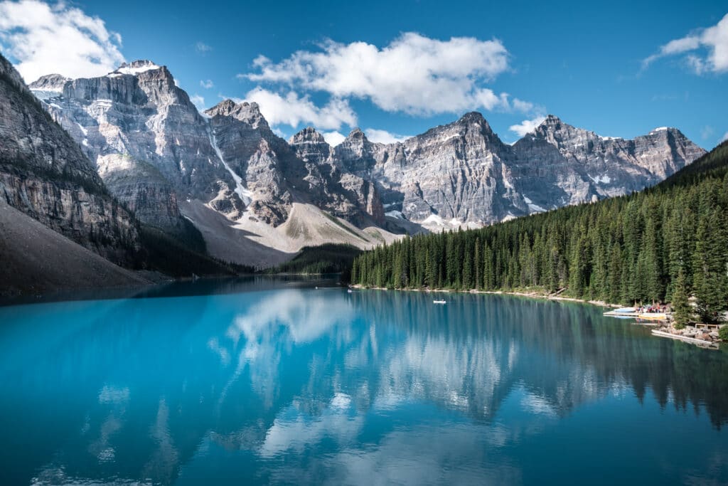 blue lake with pine trees on far shore and tall mountains in the background