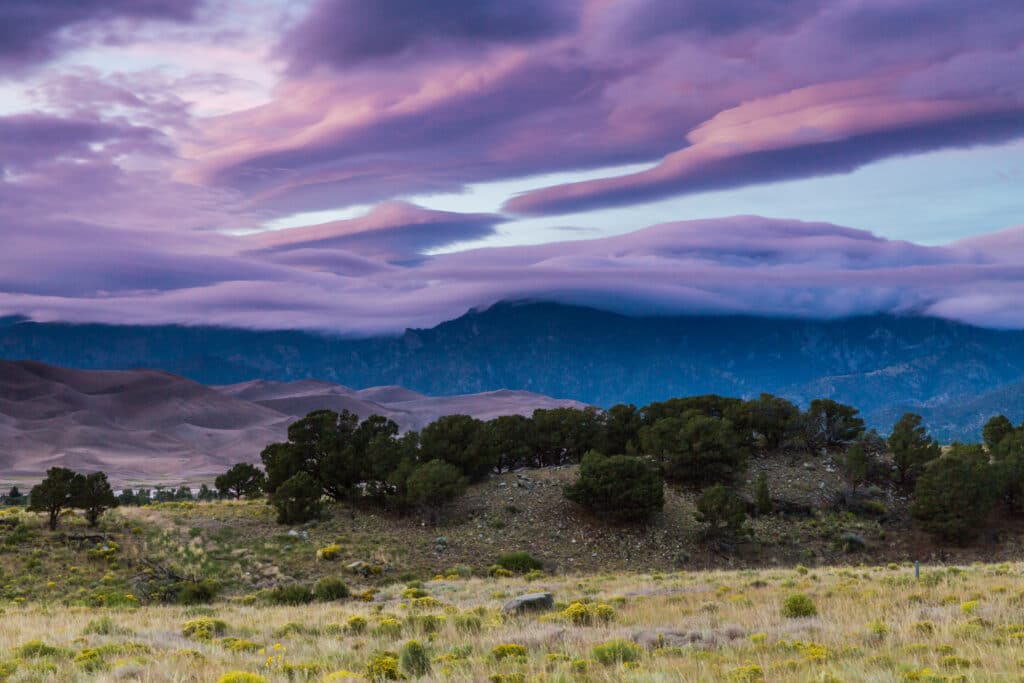 view of field in front of great sand dunes national park at sunset